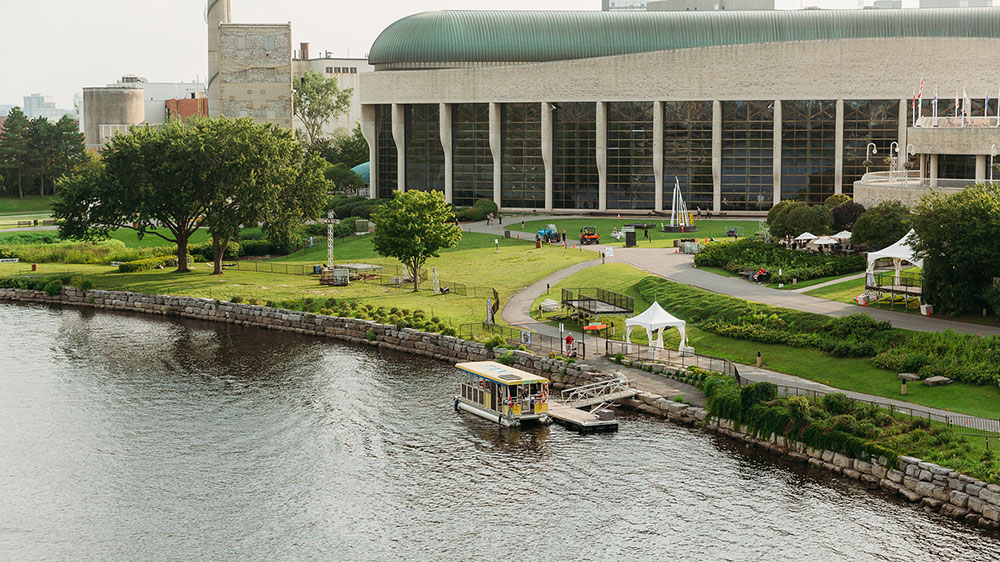 Ottawa River waterfront in Gatineau, Quebec, with a water taxi dock, green parkland, and a large modern building behind.