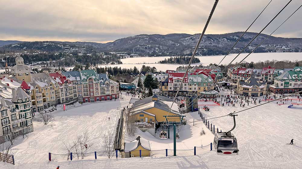 Winter view of Mont‑Tremblant village in Quebec, with colorful resort buildings, ski lifts, snow‑covered slopes, and surrounding hills.