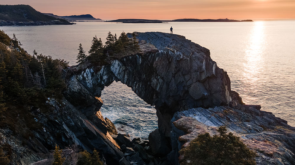 Man Hiking At Berry Head Arch At Sunrise, Along The East Coast Trail Of Newfoundland, Canada.