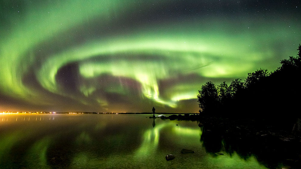 Person standing on the banks of Cold Lake watching the Northern Lights, Aurora.